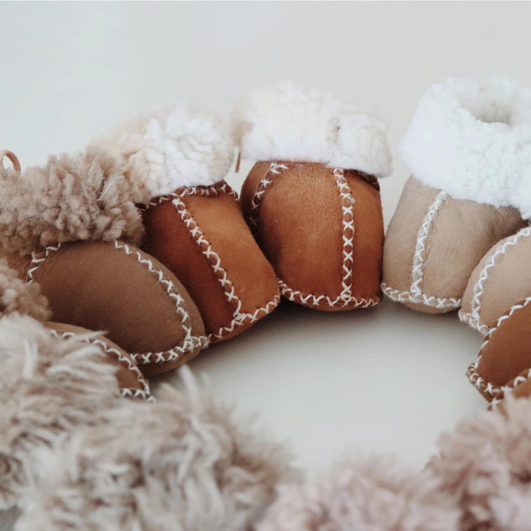 a row of sheepskin baby booties are lined up in various colours from coffee to light beige 