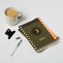 Load image into Gallery viewer, a5 sized planner, green in colour with pink, black and white detailing, featuring a black star and gold moon in the middle with &#39;around the sun weekly planner&#39; written underneath
